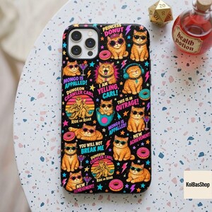 May include: A black smartphone case featuring a repeating pattern of orange cats wearing sunglasses, interspersed with pink donuts, colorful stars, and lightning bolts. The design includes text such as Princess Donut, Mongo Appalled, and Dungeon Crawler Carl.