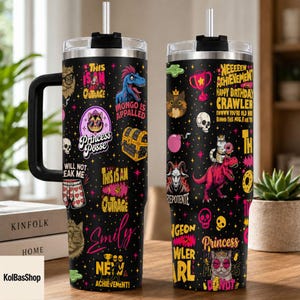 May include: Black stainless steel tumbler with a handle, featuring a variety of colorful cartoon graphics and text, including "Princess Posse" and "This is an Outrage." The tumbler has a black lid and a straw.