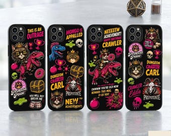 May include: Four black smartphone cases featuring colorful graphic prints of cats wearing crowns, dinosaurs, skulls, treasure chests, and trophies. The designs include text such as This Is An Outrage, Dungeon Crawler Carl, and New Achievement Happy Birthday Crawler.