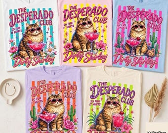 May include: Five t-shirts in white, pink, blue, lavender, and cream, each featuring a graphic of a fluffy cat wearing heart-shaped sunglasses, holding a cocktail, with the text The Desperado Club, So Fun It Hurts, and Dirty Shirley.