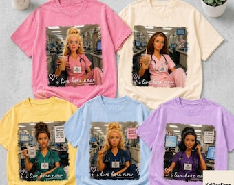 May include: Five short-sleeved crew neck t-shirts in pink, cream, yellow, light blue, and lavender. Each shirt features a graphic print of a doll dressed in scrubs within a hospital setting, holding a coffee cup, with the text I live here now.