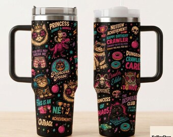 May include: Two stainless steel tumblers with black handles and clear lids, featuring a black background covered in colorful illustrations of cats, donuts, skulls, and bombs, along with text including Princess Posse, New Achievement, and Dungeon Crawler.