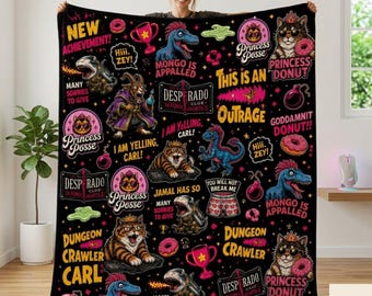 May include: A black fleece blanket featuring a repeating graphic pattern of cartoon cats, dinosaurs, and donuts. Text includes "New Achievement," "Princess Posse," "Desperado Club," "Mongo is Appalled," "Dungeon Crawler Carl," and "I am yelling, Carl!"