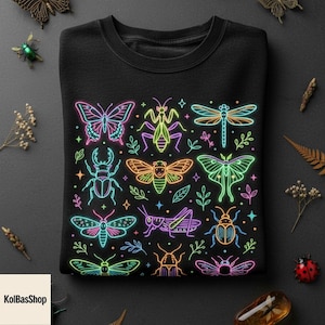 May include: A black crewneck sweatshirt featuring a vibrant neon-style graphic print of various insects including butterflies, beetles, dragonflies, and moths in bright shades of pink, blue, green, orange, and yellow, accented with small stars.