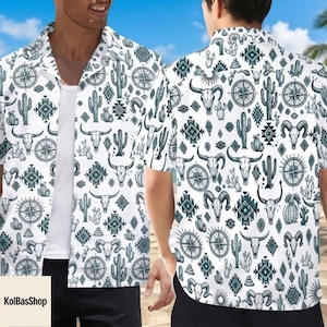 May include: White button-down shirt with a repeating pattern of cacti, bull skulls, compasses, and geometric shapes in teal. The short-sleeved shirt is worn by a person on a beach.
