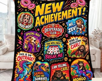 May include: A black fleece blanket featuring a colorful graphic print with the text NEW ACHIEVEMENT, DESPERADO CLUB, HOO-HOO, HI ZEV, SPECIAL BOY, YOU WILL NOT BREAK ME, VIVA LA REVOLUCION CARL, THIS IS AN OUTRAGE, JAMAL HAS NO SORRIES TO GIVE, I AM YELLING CARL, and MONGO IS APPALLED.