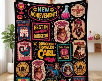 May include: A black throw blanket featuring colorful graphic patches with text including New Achievement, Best in Dungeon, Dungeon Crawler Carl, Goddamnit Donut, This is an Outrage, and Princess Donut, alongside illustrations of cats, a dinosaur, and donuts.