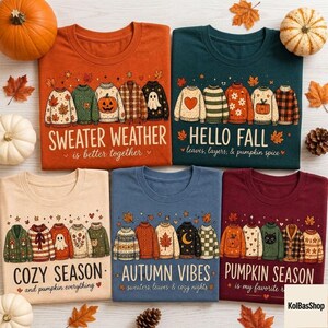Könnte beinhalten: Fünf T-Shirts in Orange, Dunkelgrün, Beige, Blau und Kastanienbraun, jeweils mit einer Grafik von fünf Pullovern und herbstlichem Text. Die Designs zeigen Illustrationen von Kürbissen, Blättern, Geistern und Katzen sowie Schriftzüge wie Sweater Weather, Hello Fall, Cozy Season, Autumn Vibes und Pumpkin Season.