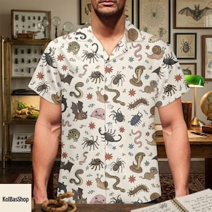 May include: A short-sleeved button-down shirt in off-white featuring a repeating pattern of various creatures including spiders, snakes, scorpions, bats, snails, centipedes, and blob-like figures, interspersed with small star-shaped icons.
