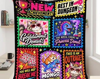 May include: A black fleece blanket featuring a grid of colorful graphic panels with text. Designs include a cat in heart-shaped glasses, a blue dragon, floral patterned shorts, and a cat wearing a crown. Text includes New Achievement, Best in Dungeon, Goddammit Donut, The Royal Court of Princess Donut, You Will Not Break Me, and Mongo is Appalled.