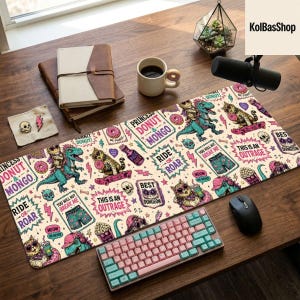 Könnte beinhalten: Eine große rechteckige Schreibtischunterlage mit einem wiederkehrenden Muster aus Cartoon-Dinosauriern, Katzen, Donuts, Totenköpfen und Blitzen. Der Text enthält Phrasen wie Princess Donut & Mongo, Ride or Roar, This is an Outrage und Best Dungeon.