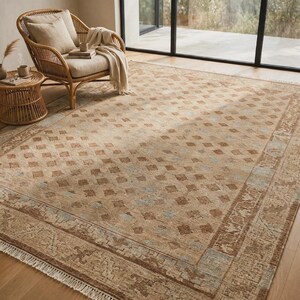 May include: A large rectangular area rug featuring a repeating diamond pattern in shades of tan, brown, and light blue. The rug has a wide decorative border with intricate motifs and short white fringe along the edges of the short sides.