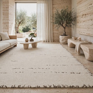 May include: A large, rectangular area rug in a soft cream color, featuring a textured surface with horizontal rows of small, dark brown dashed lines. The rug has a thick, plush pile and covers a significant portion of the floor space in the room.
