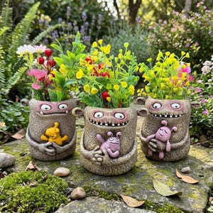 May include: Three whimsical monster-shaped planters, each holding colorful faux flowers. The planters are a textured, neutral color with cartoonish faces and arms that embrace small monster figures. The plants feature yellow, pink, and red blooms.