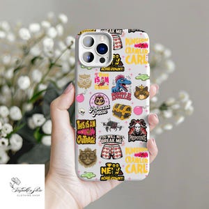 May include: A white phone case with a repeating pattern of colorful cartoon graphics and text. The graphics include a dinosaur, a treasure chest, cats, and phrases like "Princess Posse" and "Dungeon Crawler Carl".