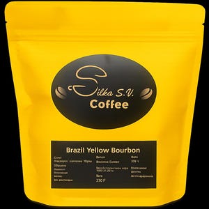 Może przedstawiać: Żółta torba na kawę z napisem "Silka S.V. Coffee" w czarnym owalu. Torba jest oznaczona jako "Brazil Yellow Bourbon" z dodatkowym tekstem i wymiarami. Torba jest zamknięta i stoi na czarnym tle.