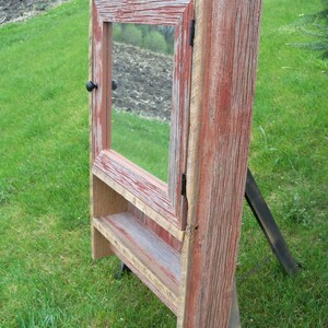 May include: A rustic wooden medicine cabinet with a red stained finish and a mirror door. The cabinet has a small shelf inside and a black knob.