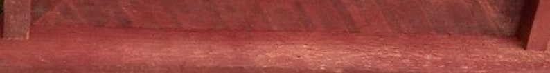 May include: A close-up of a smooth, reddish-brown wooden surface. The wood has a natural grain pattern and a slightly glossy finish.