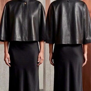 May include: A black leather cape jacket with a high collar and button fastening, worn with a black midi skirt. The model is wearing black heels. The outfit is shown from the front and back.