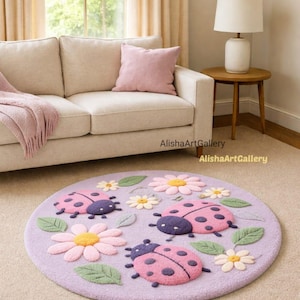 Può includere: Un tappeto rotondo color lavanda con un motivo a coccinelle e fiori. Le coccinelle sono rosa con teste viola e pois neri. I fiori sono rosa e bianchi con centri gialli. Il tappeto è su una moquette beige. Il testo "AlishaArtGallery" è visibile.