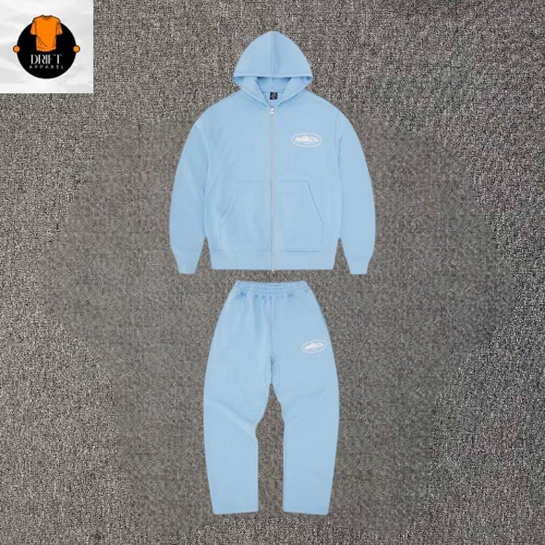 Puede incluir: Un conjunto a juego de color azul claro que consta de una sudadera con capucha y cremallera y pantalones de ch&aacute;ndal. La sudadera tiene una cremallera frontal completa, capucha y un peque&ntilde;o logotipo ovalado blanco en el pecho. El pantal&oacute;n tiene un logo.