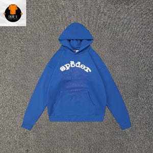 May include: A bright blue hooded sweatshirt featuring a large white arched text graphic that reads "sp&ouml;der" across the chest. Below the text is a faint, subtle spiderweb pattern. The garment includes a front kangaroo pocket and long sleeves.