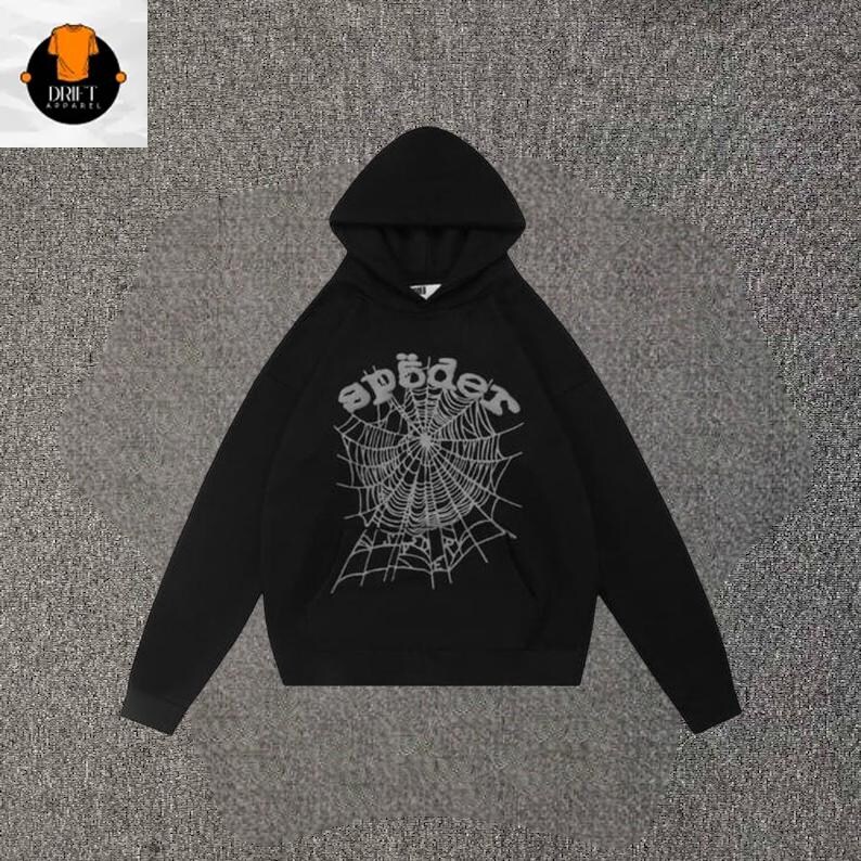 May include: A black long-sleeve hooded sweatshirt featuring a large, light gray graphic print on the front. The graphic depicts a detailed spider web design with the word "sp&ouml;der" written in a stylized, rounded font arched above the web.
