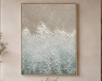 May include: A large rectangular wall art piece featuring a textured abstract ocean scene with thick white impasto paint representing crashing waves against a sandy beige shore, framed in a light wood border, displayed in a neutral-toned room.