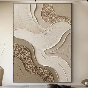 Può includere: Opera d'arte murale astratta e strutturata in tonalità neutre. L'opera presenta forme fluide e stratificate in tonalità beige, crema e marrone, con aree di texture in rilievo e puntinata. Il pezzo è incorniciato in una semplice cornice nera, creando un'estetica moderna.