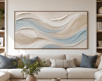 May include: A large rectangular wall art piece featuring thick, textured impasto paint in flowing, abstract waves of cream, beige, and soft blue. The artwork is framed in a thin, dark wood border and hangs centered above a large, neutral-toned sofa.
