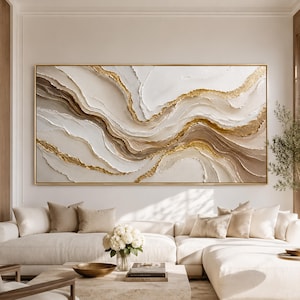 May include: A large rectangular wall art piece featuring abstract, flowing layers of white, beige, and brown paint with textured gold leaf accents. The composition consists of horizontal, wavy lines that create a sense of depth and movement.