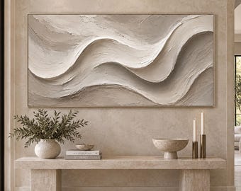 May include: A large rectangular wall art piece featuring thick, textured beige and cream paint applied in sweeping, horizontal wave patterns. The artwork is framed in a thin, light-colored border and displays a neutral, monochromatic color palette.
