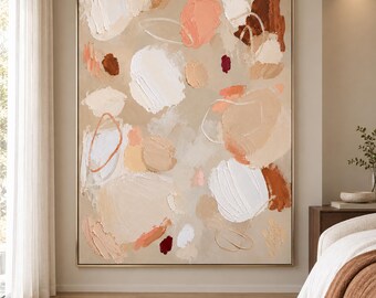 May include: A large rectangular canvas painting featuring an abstract composition of thick, textured impasto brushstrokes in shades of beige, cream, white, peach, and deep brown, framed in a thin metallic gold border hanging on a neutral wall.