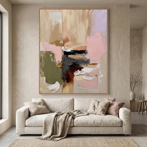 Puede incluir: Una gran pintura abstracta rectangular con pinceladas gruesas y texturizadas en tonos beige, rosa suave, verde oliva, marr&oacute;n oscuro y negro, enmarcada en madera clara y expuesta en una pared neutra sobre un sof&aacute; de color beige.