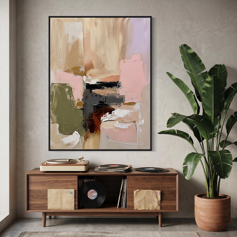Puede incluir: Una pintura abstracta rectangular en un marco negro con pinceladas gruesas y texturizadas en tonos beige, rosa suave, verde oliva, blanco y negro intenso. La obra de arte se exhibe sobre un mueble multimedia de madera con discos.