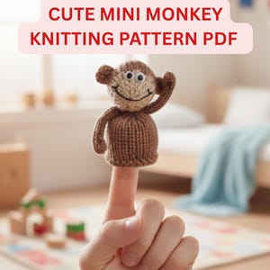 Könnte beinhalten: Eine gestrickte braune Affenpuppe mit einem lächelnden Gesicht und erhobenem Arm sitzt auf einem Finger. Der Text "CUTE MINI MONKEY KNITTING PATTERN PDF" wird in einem rosa Banner über dem Affen angezeigt. Der Hintergrund ist unscharf.