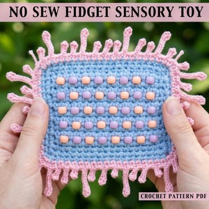 May include: A handmade, blue crochet fidget sensory toy with a pink border and fringe. The toy features rows of peach and lavender beads. The text "NO SEW FIDGET SENSORY TOY" is at the top, and "CROCHET PATTERN PDF" is at the bottom.