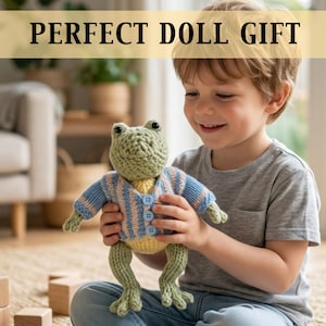 May include: A knitted frog doll with a light green head, yellow body, and blue and beige striped sweater. The doll has button details and is being held by a child. The text "PERFECT DOLL GIFT" is displayed above the doll.