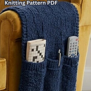 Puede incluir: Organizador de sillón tejido en azul marino con tres bolsillos. El organizador está sobre un sillón amarillo. Los bolsillos contienen un crucigrama, un bolígrafo y un mando a distancia. El texto superior dice "ARM CHAIR ORGANIZER Knitting Pattern PDF."