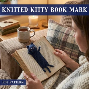 Könnte beinhalten: Ein marineblauer, gestrickter Katzen-Lesezeichen liegt auf den Seiten eines Buches. Das Lesezeichen hat weiße, gestickte Details für Augen und Mund. Der Text "KNITTED KITTY BOOK MARK" steht oben und "PDF PATTERN" unten im Bild.
