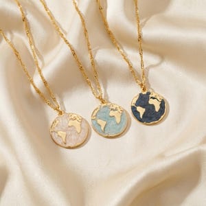 May include: Three gold necklaces with globe pendants. Each pendant features a different colour scheme: pale pink, light blue, and navy blue. The necklaces are displayed on a cream satin surface. The chains have a twisted design.