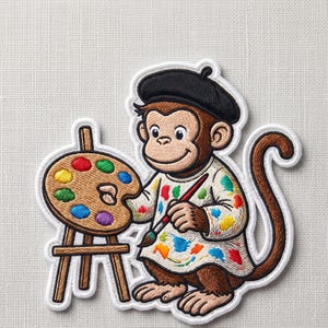 May include: An embroidered patch featuring a brown monkey wearing a black beret and a white smock splattered with colorful paint. The monkey holds a paintbrush and stands next to a wooden easel holding an oval palette with red, yellow, blue, green, and purple paint spots.