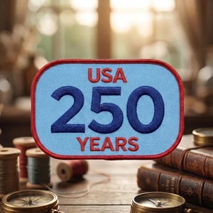 May include: A rectangular patch with a light blue background and a red border. The text "USA 250 YEARS" is embroidered in dark blue. The patch is likely a commemorative item, possibly for a historical event or anniversary.