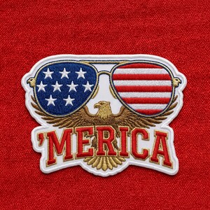 May include: An embroidered patch featuring a golden eagle with wings spread, wearing sunglasses with a blue star-spangled banner pattern on the left lens and red and white stripes on the right lens, with the red text 'MERICA' below the eagle.