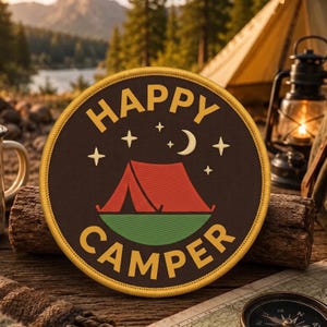 May include: A circular embroidered patch with a dark brown background, a yellow border, and the text HAPPY CAMPER in yellow. The design features a red tent on a green base, a yellow crescent moon, and four-pointed stars in the night sky.