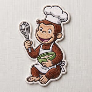 May include: An embroidered patch featuring a brown monkey wearing a white chef hat and a white apron. The monkey is smiling and holding a silver wire whisk in one hand and a green mixing bowl containing a light-colored substance in the other.