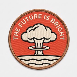 May include: A circular embroidered patch with a red background and a brown stitched border. It features a white mushroom cloud graphic with a black outline and wavy white lines at the base. The text THE FUTURE IS BRIGHT is stitched in white.
