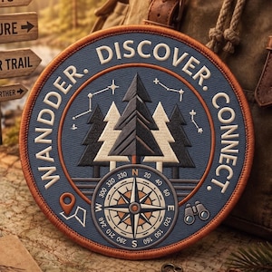 May include: A circular embroidered patch featuring a blue background with a forest of dark and light pine trees, a compass, and constellations. The text WANDER. DISCOVER. CONNECT. circles the border, accompanied by a map pin and binoculars.