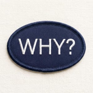 May include: An oval-shaped navy blue embroidered patch featuring the word WHY? stitched in white capital letters. The patch has a dark blue stitched border around the entire edge, creating a clean and defined outline for the fabric accessory.