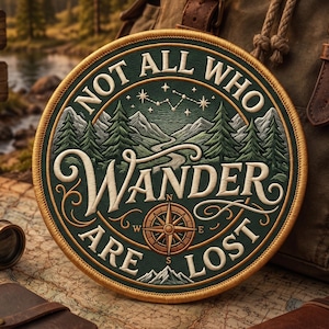 May include: A circular embroidered patch featuring a dark green background with a mountain landscape, pine trees, and a starry sky. The text reads NOT ALL WHO WANDER ARE LOST in white lettering, with a central brown compass and gold border.